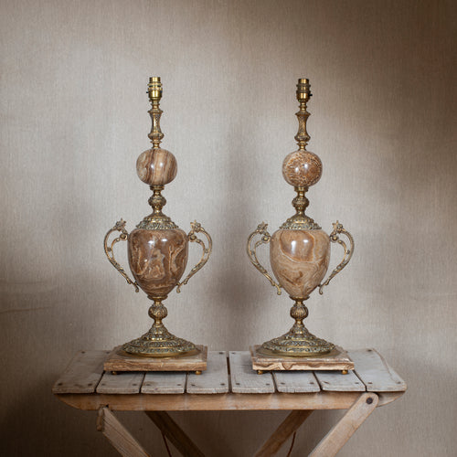 Two ornate lamps on a wooden table against a plain wall