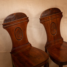 Load image into Gallery viewer, Two wooden chairs with intricate back designs against a beige wall.
