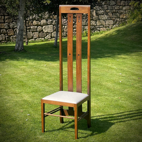 Wooden chair with a white cushion on a grassy area with a stone wall in the background